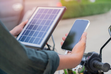 Back view of man connects solar panel to mobile phone for charge, eco-friendly urban transportation.