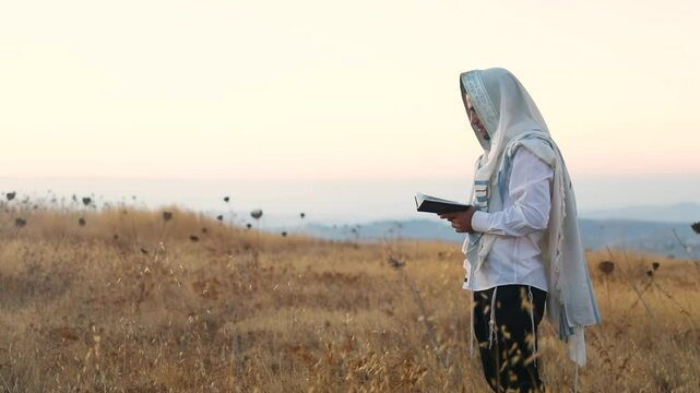 A jew prays in a field at sunrise, with tallit and Sidur. Tfilat Shacharit.