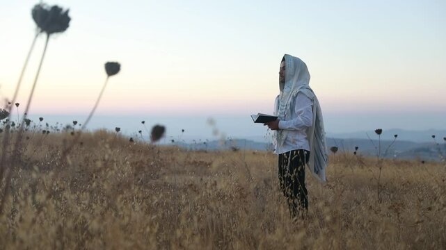 A jew prays in a field at sunrise, with tallit and Sidur. Tfilat Shacharit.