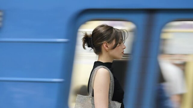 Beautiful brunette stands at the metro station waiting for the train to arrive