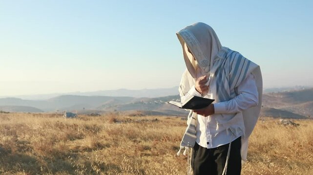 A jew prays in a field at sunrise, with tallit and Sidur. Tfilat Shacharit.