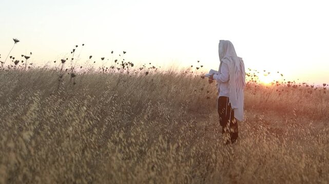 A jew prays in a field at sunrise, with tallit and Sidur. Tfilat Shacharit.