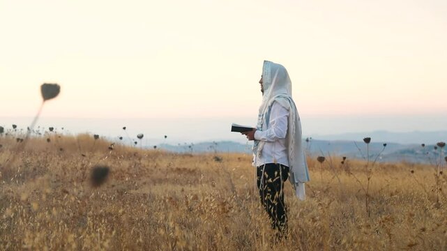 A jew prays in a field at sunrise, with tallit and Sidur. Tfilat Shacharit.