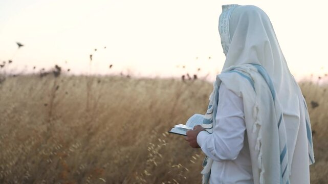 A jew prays in a field at sunrise, with tallit and Sidur. Tfilat Shacharit.