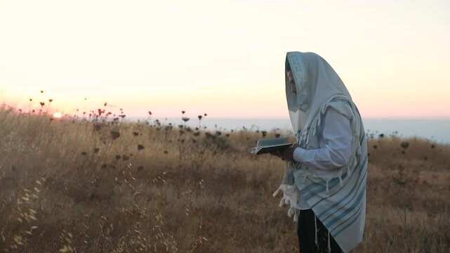 A jew prays in a field at sunrise, with tallit and Sidur. Tfilat Shacharit.