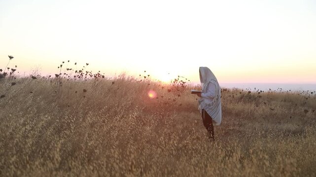 A jew prays in a field at sunrise, with tallit and Sidur. Tfilat Shacharit.