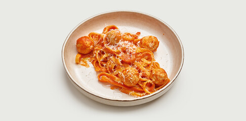A classic Italian dish of tagliatelle pasta with meatballs and tomato sauce is presented on a white plate. The pasta is cooked al dente and the meatball