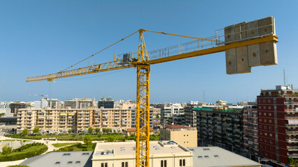 Aerial view of a yellow industrial tower crane operating in high building construction site. These large machines allow the concrete plates weight balance. City development concept. 