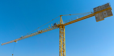 Aerial view of a yellow industrial tower crane operating in high building construction site. These large machines allow the concrete plates weight balance. City development concept. 