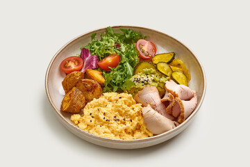 A balanced and healthy breakfast bowl filled with scrambled eggs, roasted potatoes, fresh salad, and sliced ham. The bowl is topped with avocado and sesame seeds.