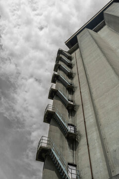 A towering industrial silo stretches upward toward the sky, with an ominous cloud backdrop, symbolizing industrialization, human ambition, and the grit of hard work.