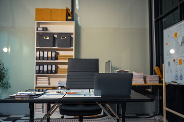 An empty office desk at night with a laptop displaying a business chart, balance sheet, loan calculator, graphs, and monthly budget stats. Blue and black tones, leather office chair.