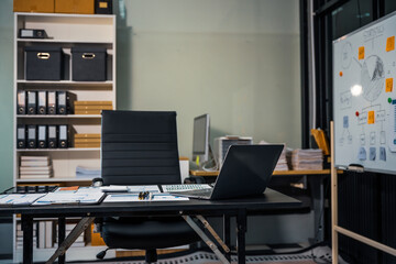 An empty office desk at night with a laptop displaying a business chart, balance sheet, loan calculator, graphs, and monthly budget stats. Blue and black tones, leather office chair.