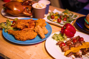 An empty office desk at night during Halloween, decorated with a pumpkin toy, paper coffee cup, BBQ grill, fried chicken, salads, apples, vegetables, and RGB lights creating a festive atmosphere.