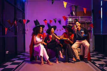 Asian friends, middle-aged man and young woman, enjoy Halloween office party with vampire costumes, fried chicken, grilled food, grape wine, champagne, RGB lights, festive decorations in the night.