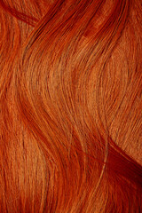Red hair close-up as a background. Women's long orange hair. Beautifully styled wavy shiny curls....