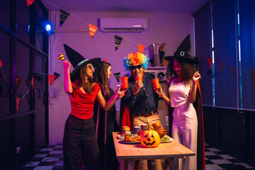 Asian friends, middle-aged man and young woman, enjoy Halloween office party with vampire costumes, fried chicken, grilled food, grape wine, champagne, RGB lights, festive decorations in the night.