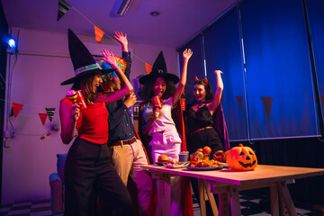 Asian friends, middle-aged man and young woman, enjoy Halloween office party with vampire costumes, fried chicken, grilled food, grape wine, champagne, RGB lights, festive decorations in the night.