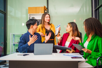 Asian colleagues, middle-aged man and young woman, happily collaborate in office workplace. They gather around laptop, discussing project management, startup plans, teamwork paper stacks on desk.