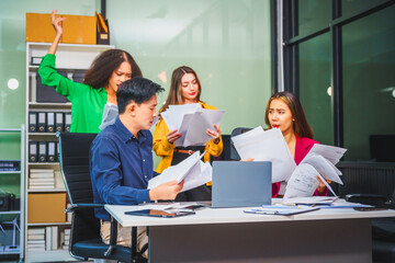 Asian colleagues, middle-aged man and young woman, happily collaborate in office workplace. They gather around laptop, discussing project management, startup plans, teamwork paper stacks on desk.