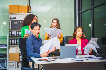 Asian colleagues, middle-aged man and young woman, happily collaborate in office workplace. They gather around laptop, discussing project management, startup plans, teamwork paper stacks on desk.