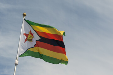 Flag of Zimbabwe, Zimbabwe, national symbol of Zimbabwe. Flag of Zimbabwe fluttering in blue sky. Independence Day. Flag of Zimbabwe, close-up. Great for news.