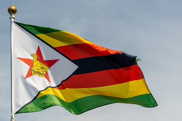 Flag of Zimbabwe, Zimbabwe, national symbol of Zimbabwe. Flag of Zimbabwe fluttering in blue sky....