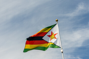 Flag of Zimbabwe, Zimbabwe, national symbol of Zimbabwe. Flag of Zimbabwe fluttering in blue sky. Independence Day. Flag of Zimbabwe, close-up. Great for news.