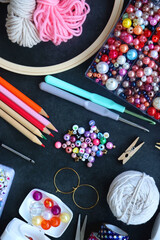 Colorful beads, coloring pencils, glitter, needles, string, hoop, tape and scissors on dark...