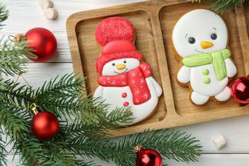 Delicious cookies in shape of snowmen, marshmallows and Christmas decor on white wooden table, flat lay