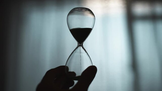 ガラス製の砂時計を持つ人の手元シルエット
