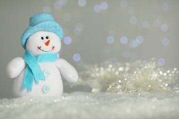 Cute decorative snowman on artificial snow against blurred lights. Space for text
