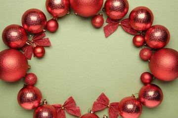 Christmas decor. Frame of shiny baubles and bows on green background, flat lay. Space for text
