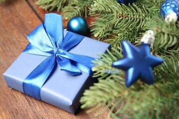 Fir tree branches with Christmas decor and gift box on wooden table, closeup