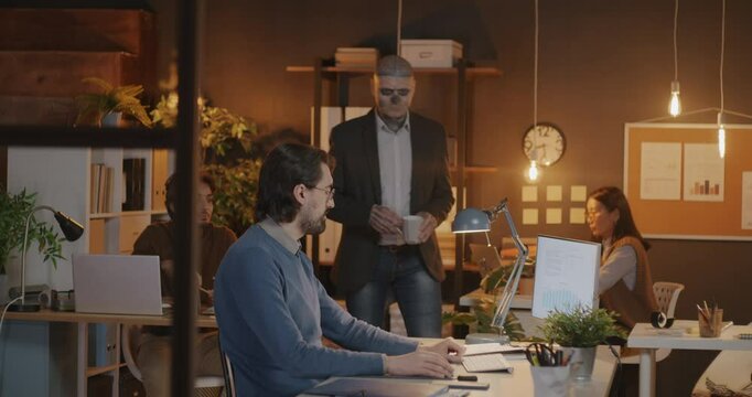 Businessman with creative tattoo multicultural company manager talking to diverse group of employees in office in evening. Inclusive workplace and job concept.