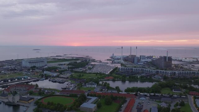 Copenhagen harbor glows in the warm light of sunset. Boats gently rocking in the water, while the amager power station rises against a vibrant, colorful sky