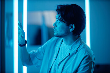 Side view portrait of Asian man touching blue neon light strips during modern art show in museum enjoying multisensory experience