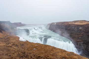 The majestic Gullfoss waterfall in Iceland, formed by the Hvita river cascading down two tiers into a narrow canyon. The powerful water flow and misty spray create a breathtaking sight.