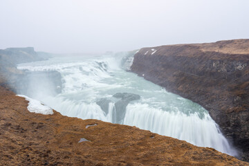 The majestic Gullfoss waterfall in Iceland, formed by the Hvita river cascading down two tiers into a narrow canyon. The powerful water flow and misty spray create a breathtaking sight.