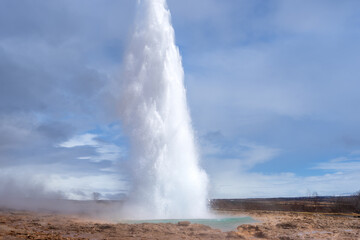 Tourists marvel at the Strokkur geyser erupting, sending a plume of steam and water high into the air. This geothermal wonder is a popular attraction in Iceland. Geysir Geothermal Area, Iceland.