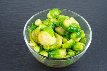 Cooked organic brussels sprouts in glass jare on black background.