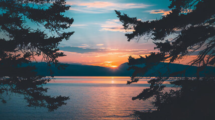 A photo of a peaceful sunset scene over a calm lake or sea, framed by the silhouettes of dark trees. The sun has just set behind distantmountains, casting soft orange and blue hues across the sky. The