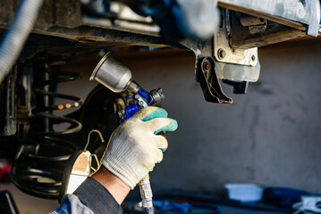 Man spraying an anti-corrosion compound on bottom of car.