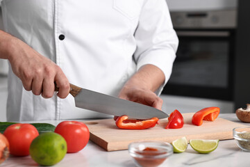 Professional chef cutting bell pepper at white marble table in kitchen, closeup