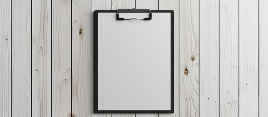 A black clip and a white blank note paper are attached to a wooden panel. with copy space image. Place for adding text or design