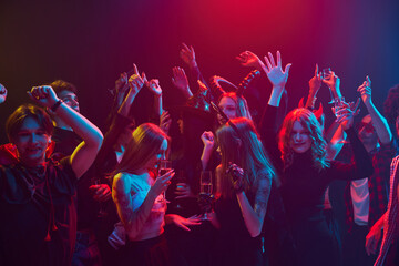 Lively group of young people, men and women attending night club for Halloween party, showing off their costumes and enjoying night filled with music and dancing. Concept of Halloween, holiday