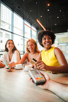 Vertical. Young African American woman is settling her bill with a contactless creditcard at a restaurant. She smiles as she hands over her credit card to complete the payment with the cashier