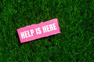 Help is here message written on ripped torn pink paper piece on green grass background. Conceptual...