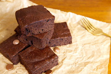 Brownies and fork on brown paper with a wooden table. Close-up piece of chocolate brownie with copy space. Dessert, square, food texture, and homemade concepts. Brownie background with baking paper.