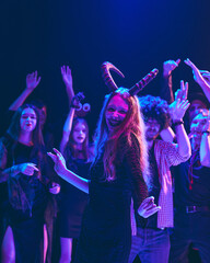 Group of friends in creative Halloween costumes celebrating with laughter and music, cheerfully dancing at dimly lit nightclub. Concept of Halloween, holiday, party, leisure